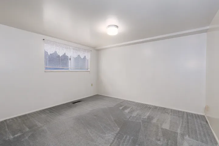 Carpeted room with white walls, a single window, and an overhead flush-mount light fixture
