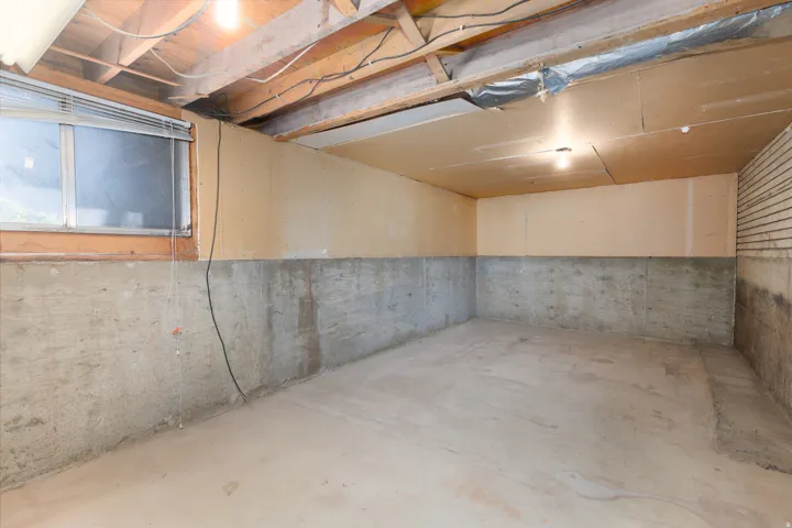 Unfinished lower level space with concrete flooring, exposed ceiling joists, and a partial window
