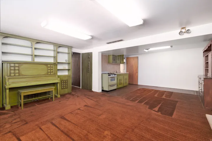 Spacious room featuring broadloom carpeting, built-in shelving, and a compact kitchen area with a gas range and cabinetry