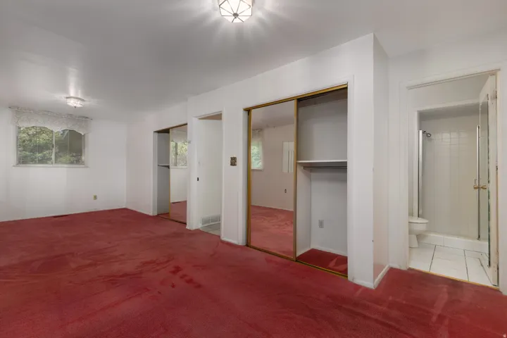 Spacious room featuring red carpeting, white walls, and a window with natural light