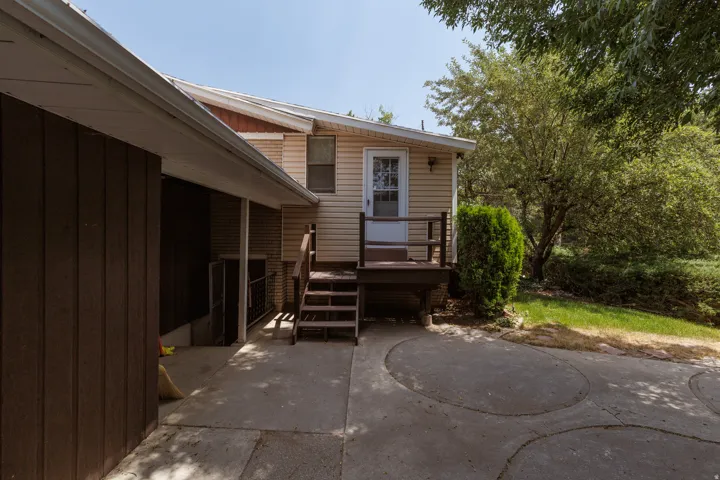 Rear exterior featuring tan siding, a brown wood deck, and a glass-paneled door