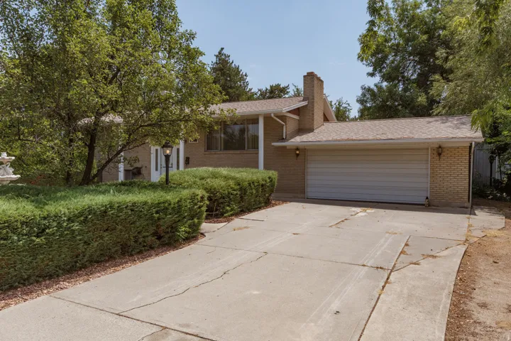Brick exterior with an attached garage, featuring a concrete driveway and lush hedges