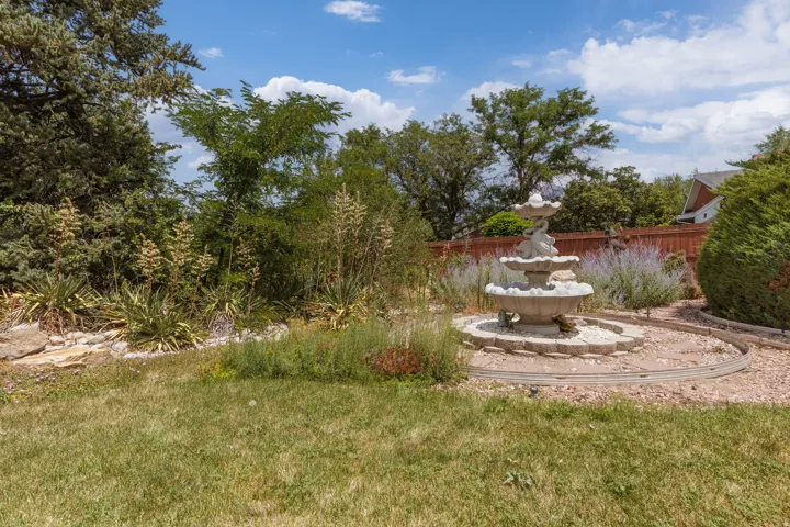 Backyard featuring a tiered stone fountain, garden beds with various plantings, and a wooden privacy fence
