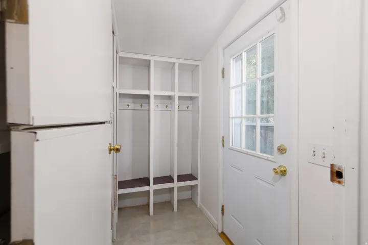 Entryway with built-in cubby storage, white shaker-style door with glass pane, brass-finish hardware, and light-toned flooring