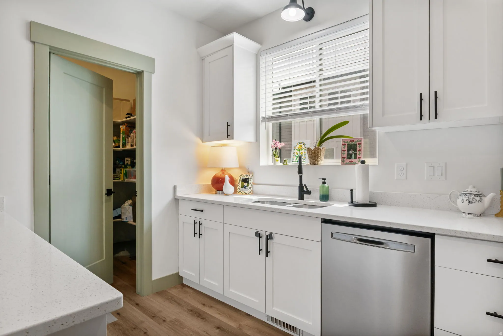 White shaker cabinetry with matte black hardware, stainless steel dishwasher, undermount sink with matte black faucet, and light-toned countertops