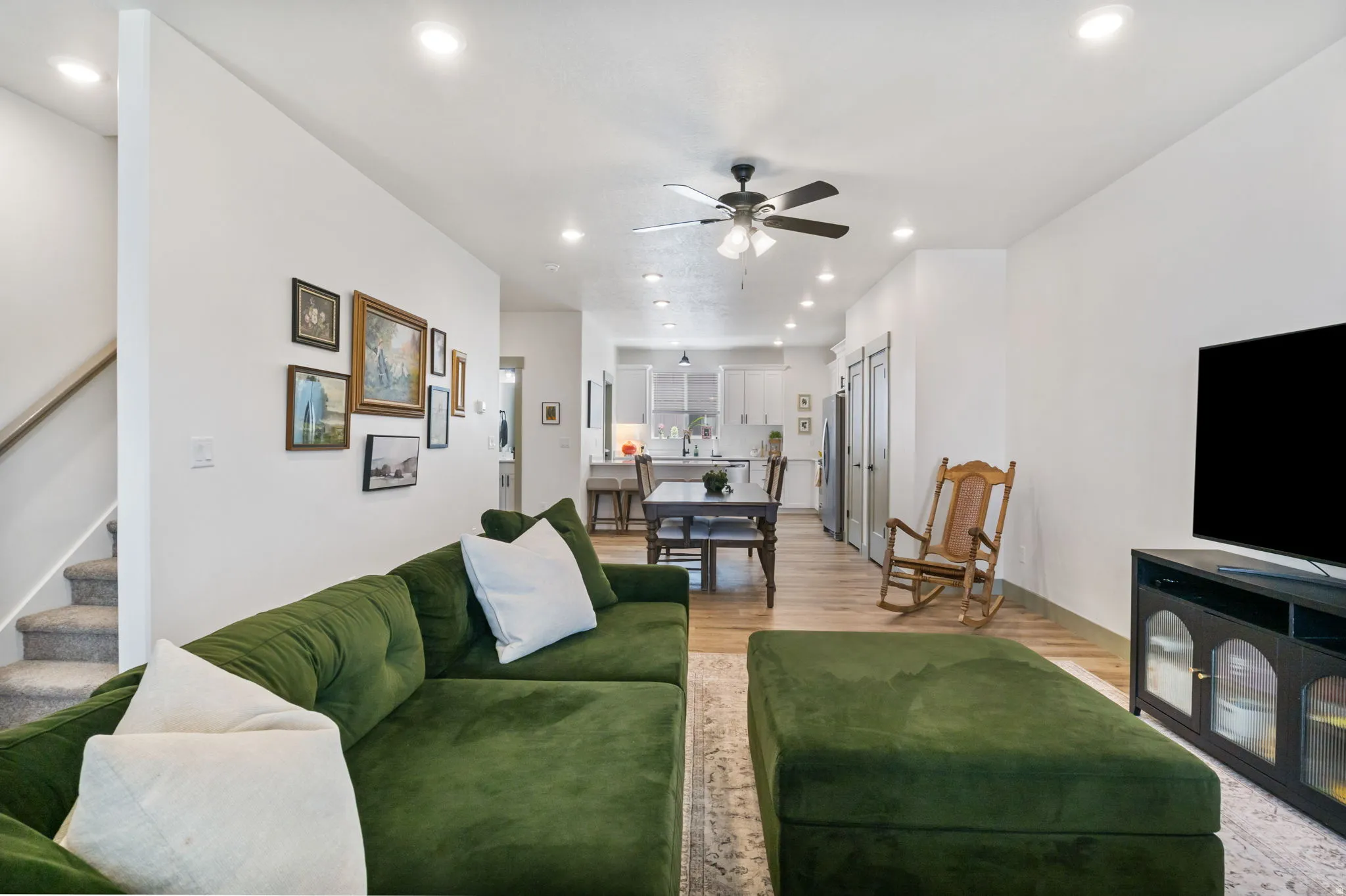 Recessed lighting, ceiling fan, wood-finish flooring, two-panel interior doors, and a carpeted staircase with wood handrail