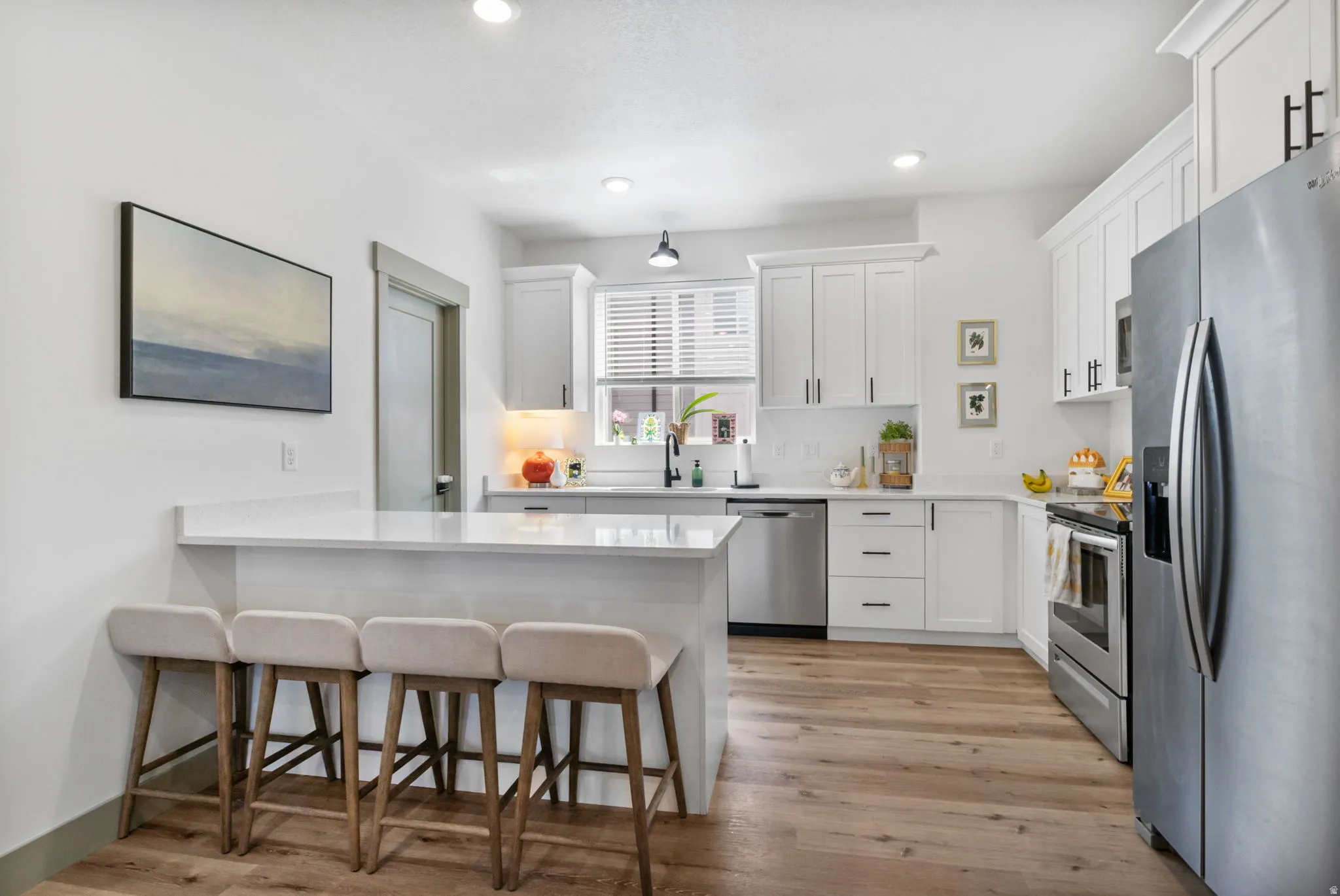 White shaker cabinetry with matte black hardware, stainless steel appliances, wood-finish flooring, recessed lighting, and a white countertop island