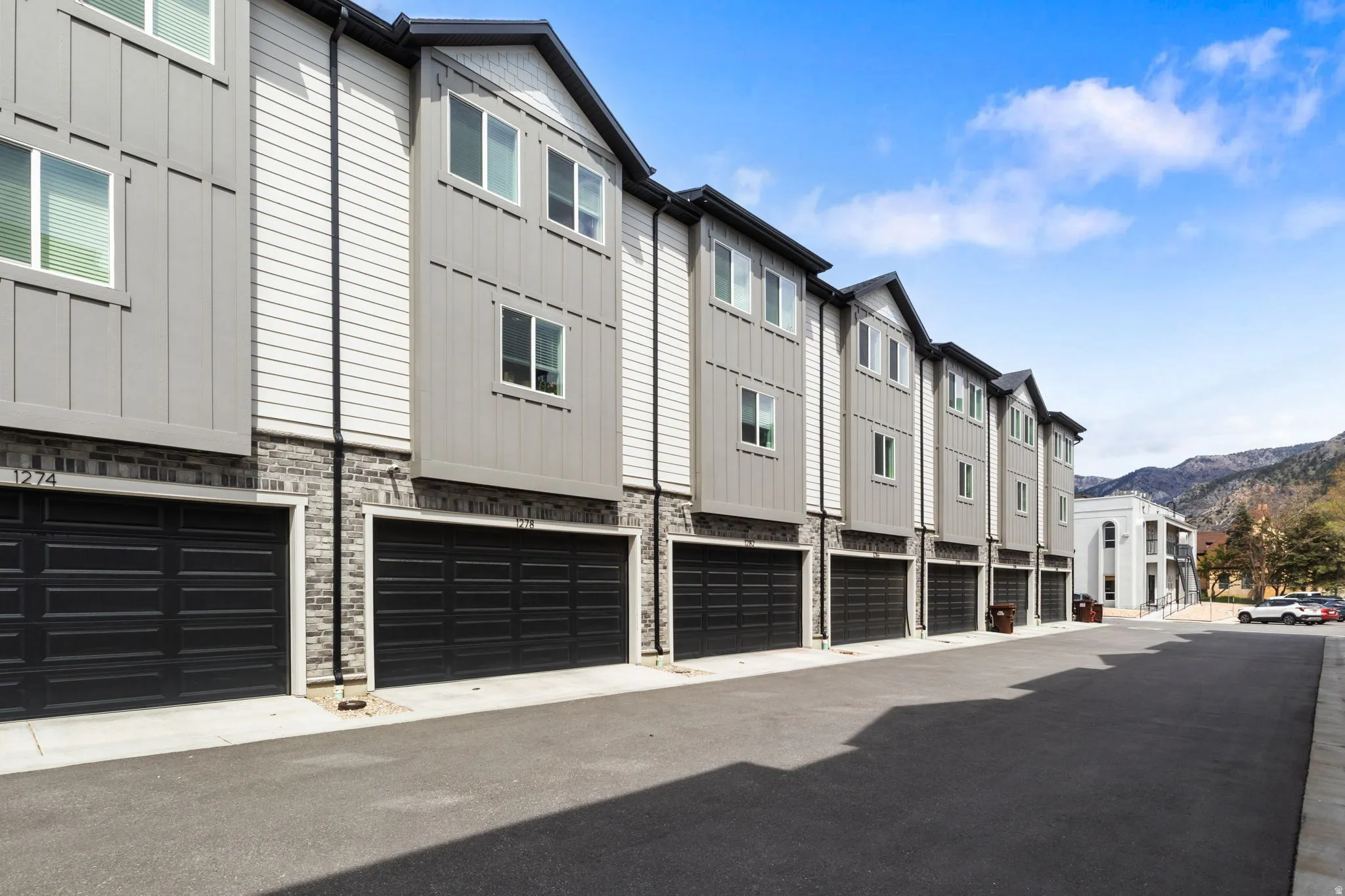 Multi-level townhome featuring a mixed-material exterior, black garage doors, and white-framed windows