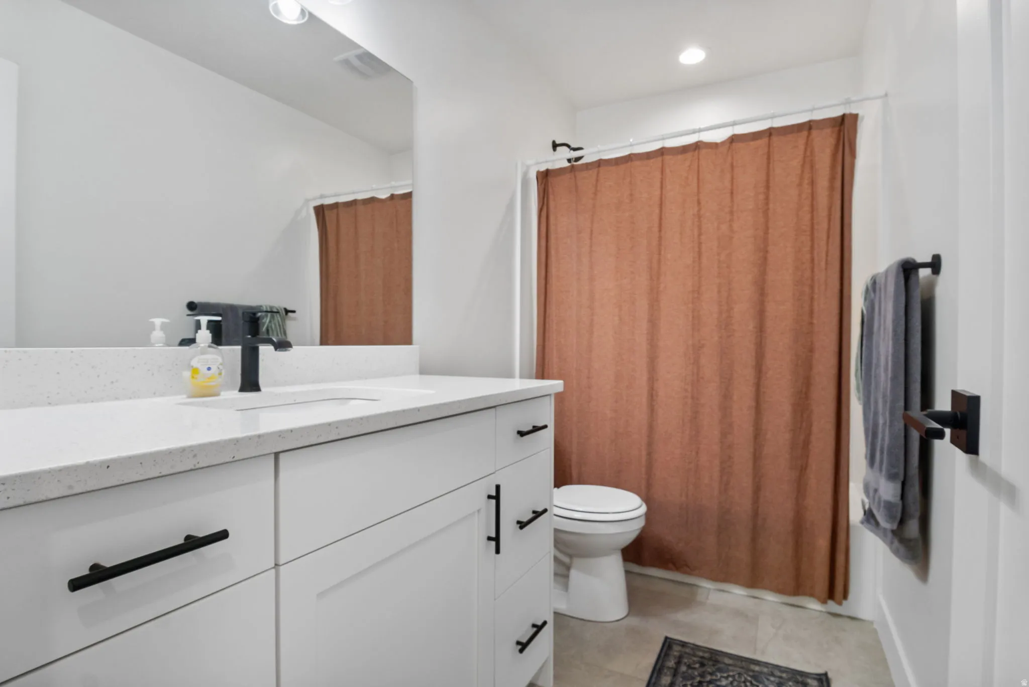 White cabinetry with matte black hardware, integrated sink, and a speckled white countertop