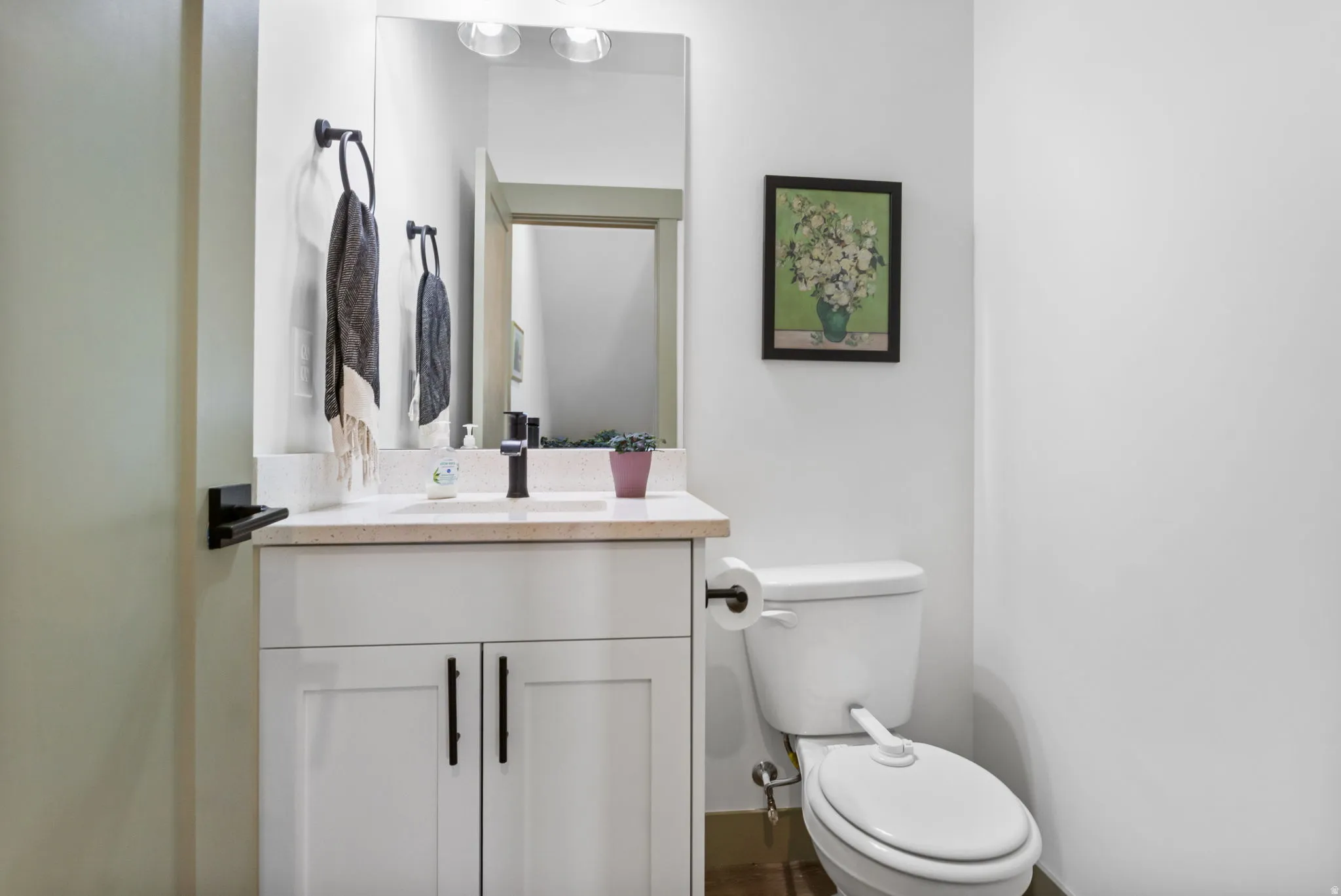 Half-bath features a white vanity with dual cabinet doors and matte black hardware, under-mount sink, and light-toned countertop