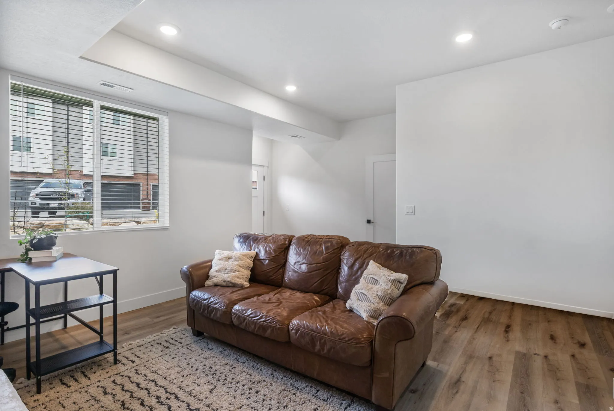 Recessed lighting, wood-finish flooring, white walls, and a large window with blinds
