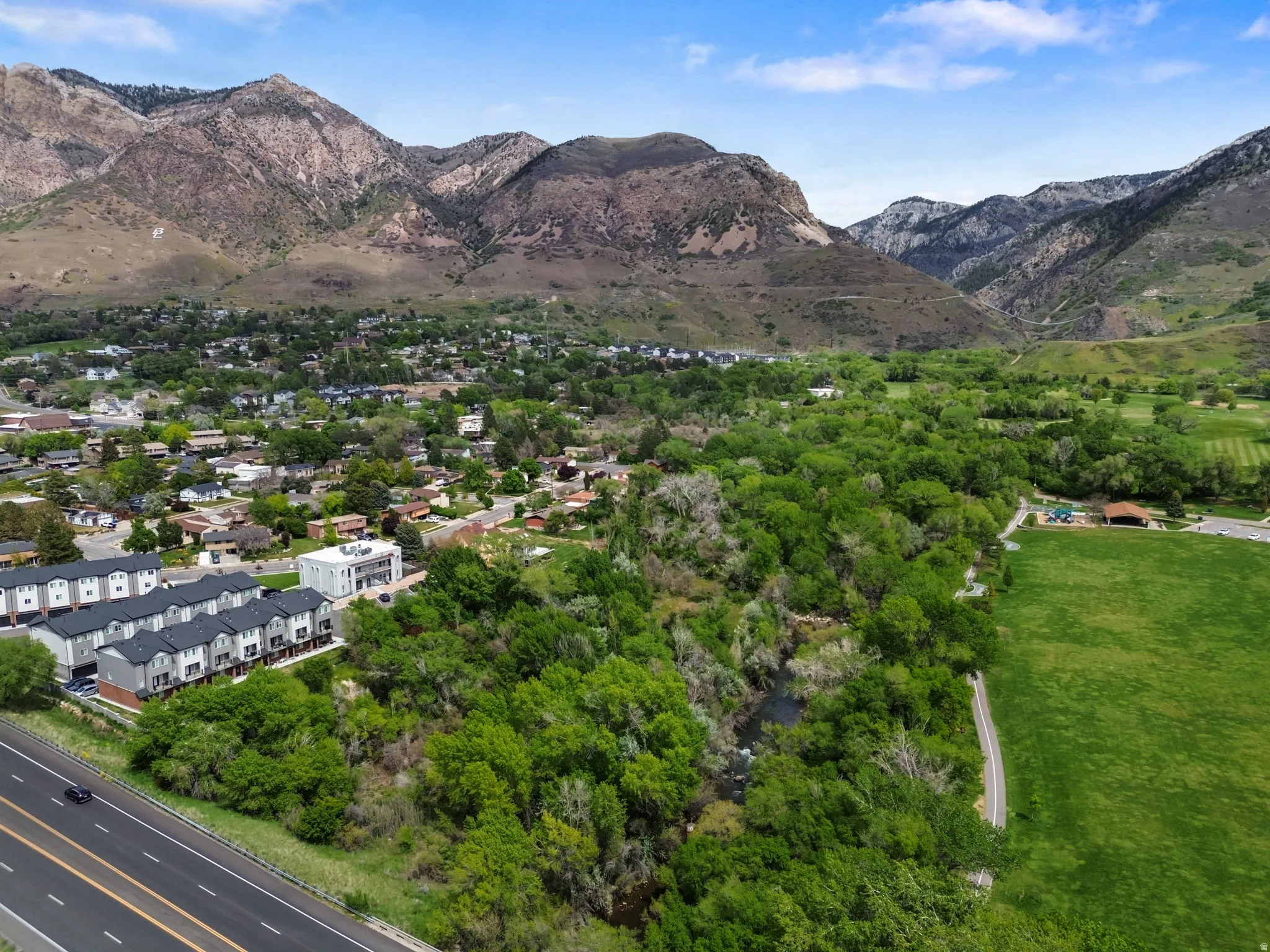 Mountainous terrain, lush green landscape, established residential area, modern townhomes, and a developed roadway