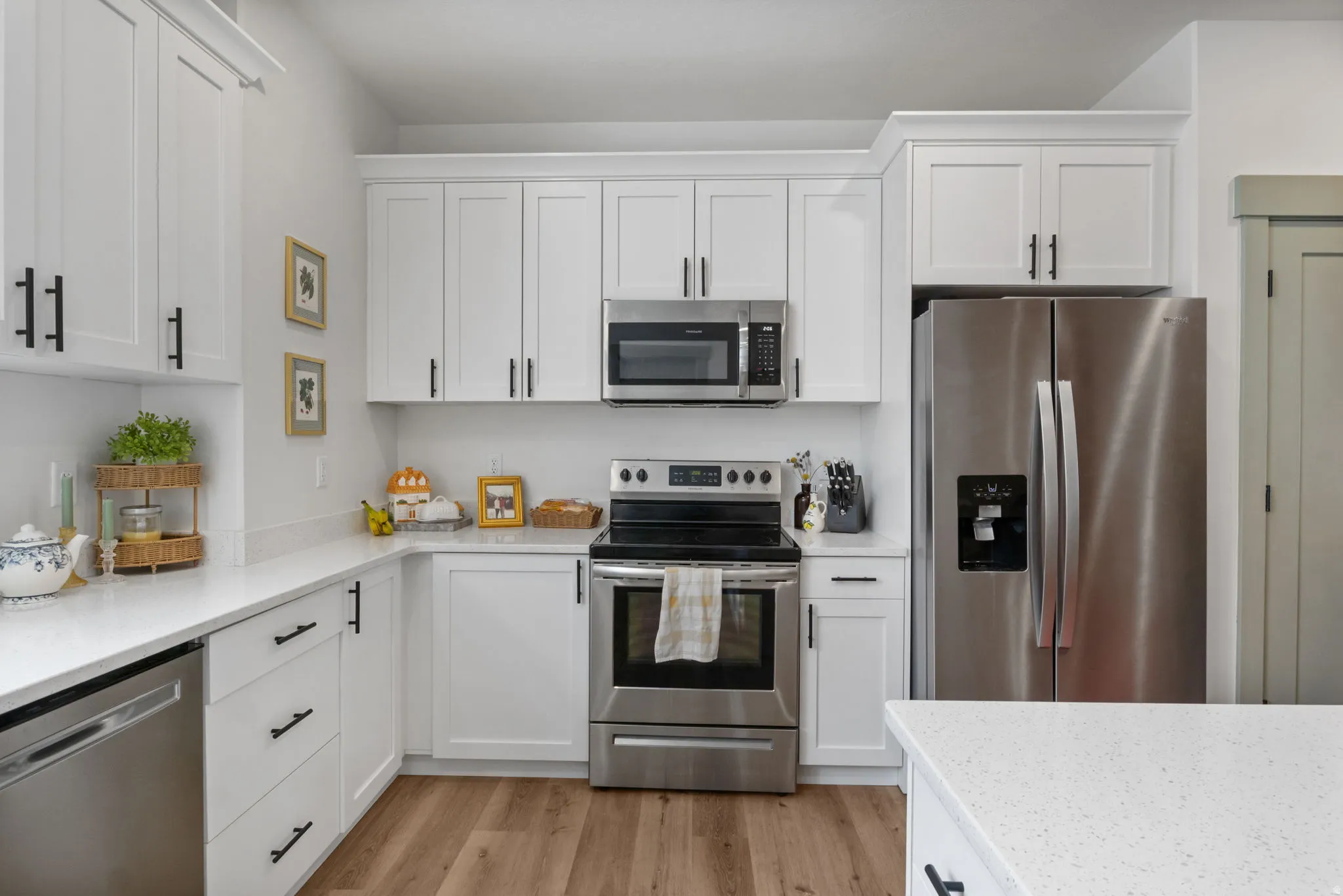 White shaker-style cabinetry, stainless steel appliances, quartz countertops, wood-finish flooring, and matte black hardware