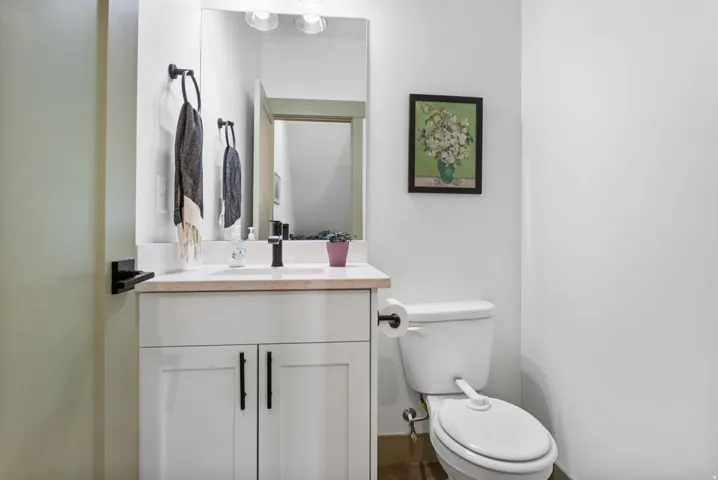 Half-bath features a white vanity with dual cabinet doors and matte black hardware, under-mount sink, and light-toned countertop