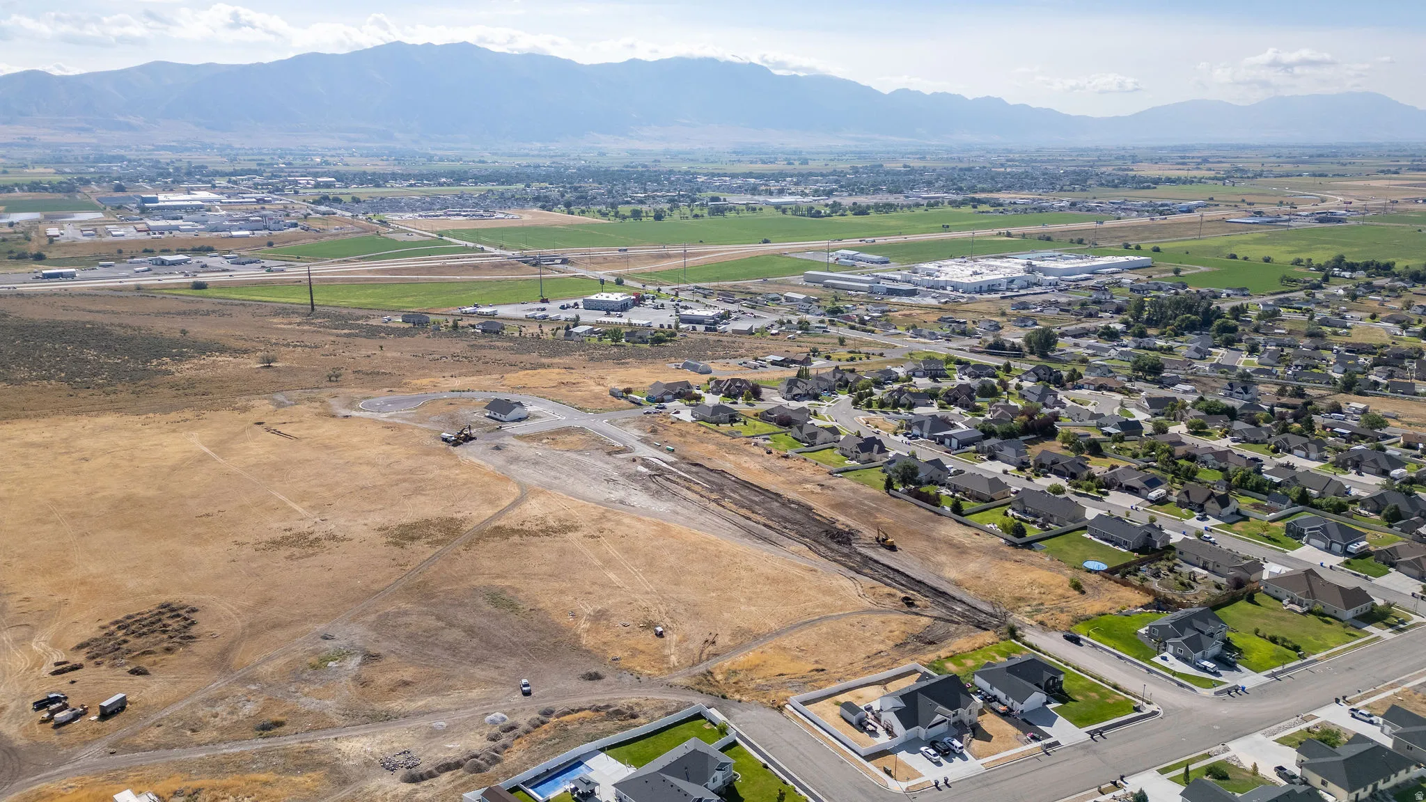 Mountain backdrop, residential development, established neighborhood, agricultural fields, distant commercial structures