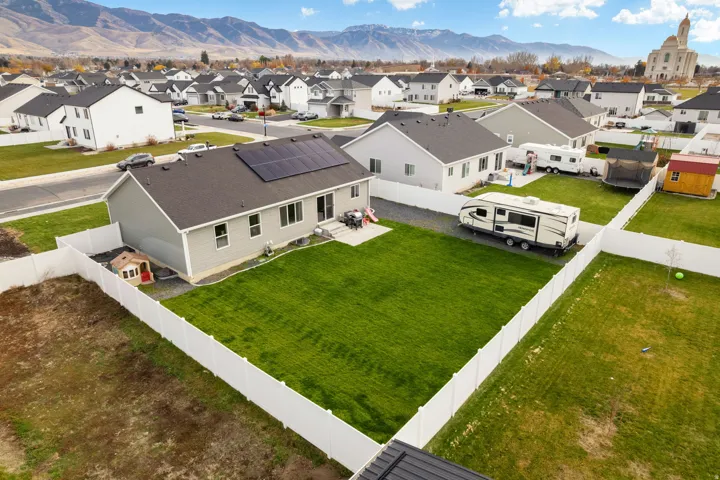 Rear exterior featuring a manicured lawn, white privacy fencing, and solar panels