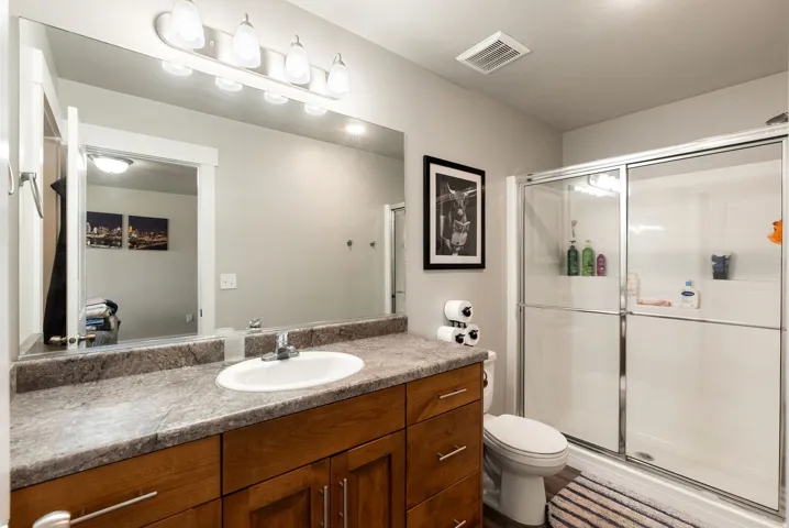 Wood-finish vanity with an integrated sink, broad mirror, and a shower with sliding glass doors