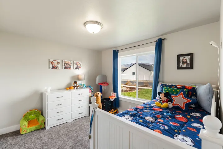 White paneled bed frame, large window, overhead flush mount light fixture, light gray walls, and gray carpet