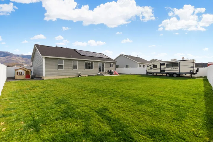 Expansive fenced backyard with a green lawn, mountain backdrop, and solar panels on the roof