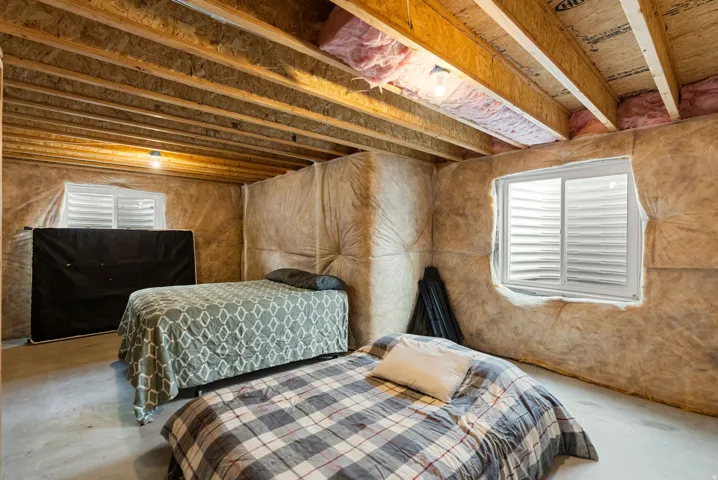 Unfinished basement space with exposed joists, insulation-lined walls, two visible egress windows, and a concrete floor
