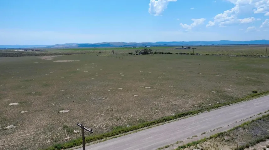 Expansive open land with distant structures, a gravel road, and mountainous terrain