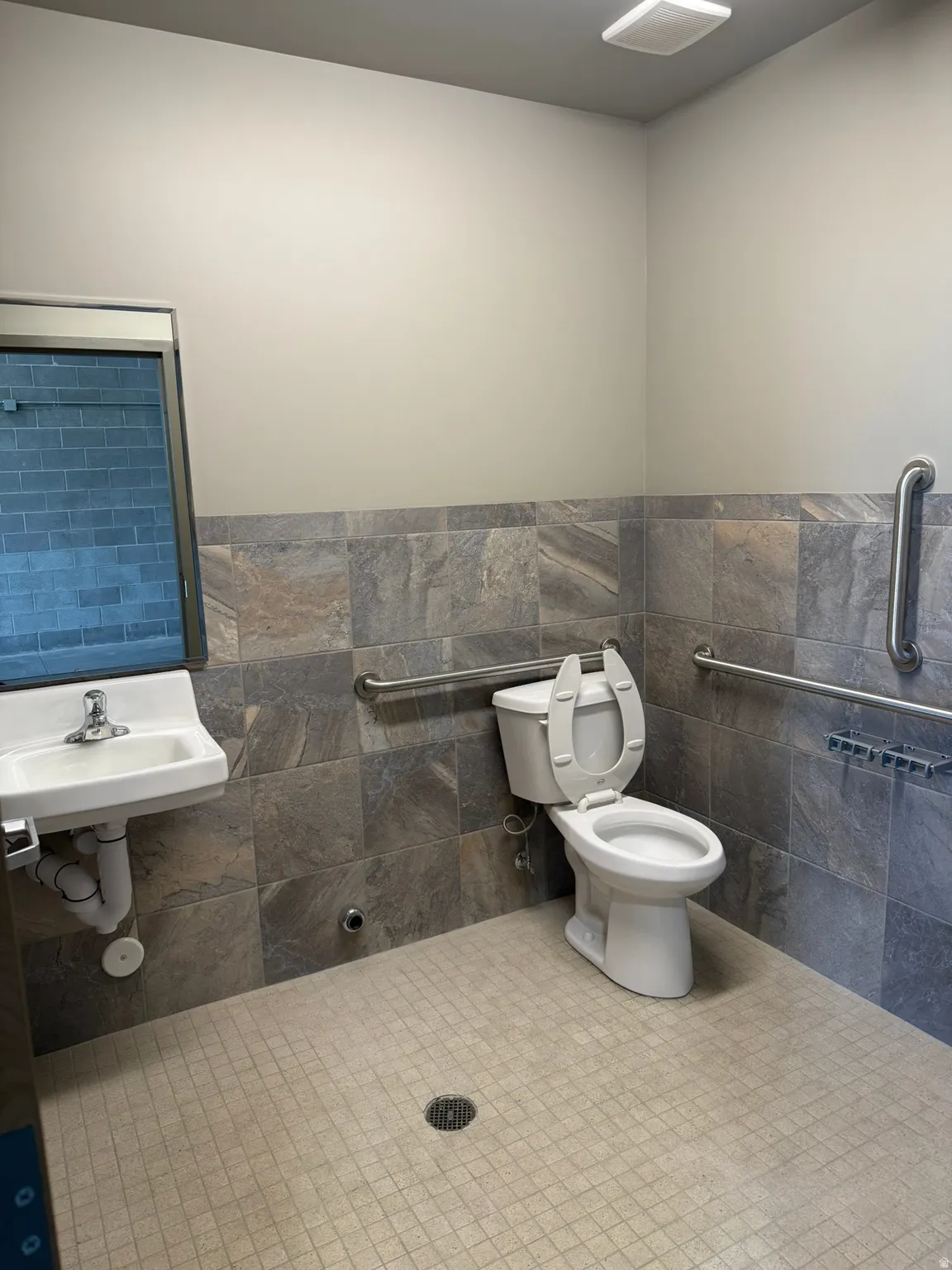 Tile wainscoting with integrated grab bars, rectangular wall-mounted sink, and mosaic tile flooring