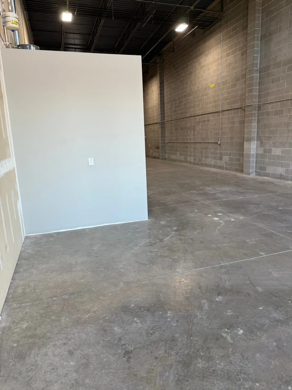 Concrete block wall construction, exposed ceiling structure, industrial-style lighting, concrete flooring, partially finished drywall partitions