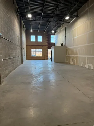 Spacious interior with exposed steel beam ceiling, concrete flooring, and ample natural light from multiple windows