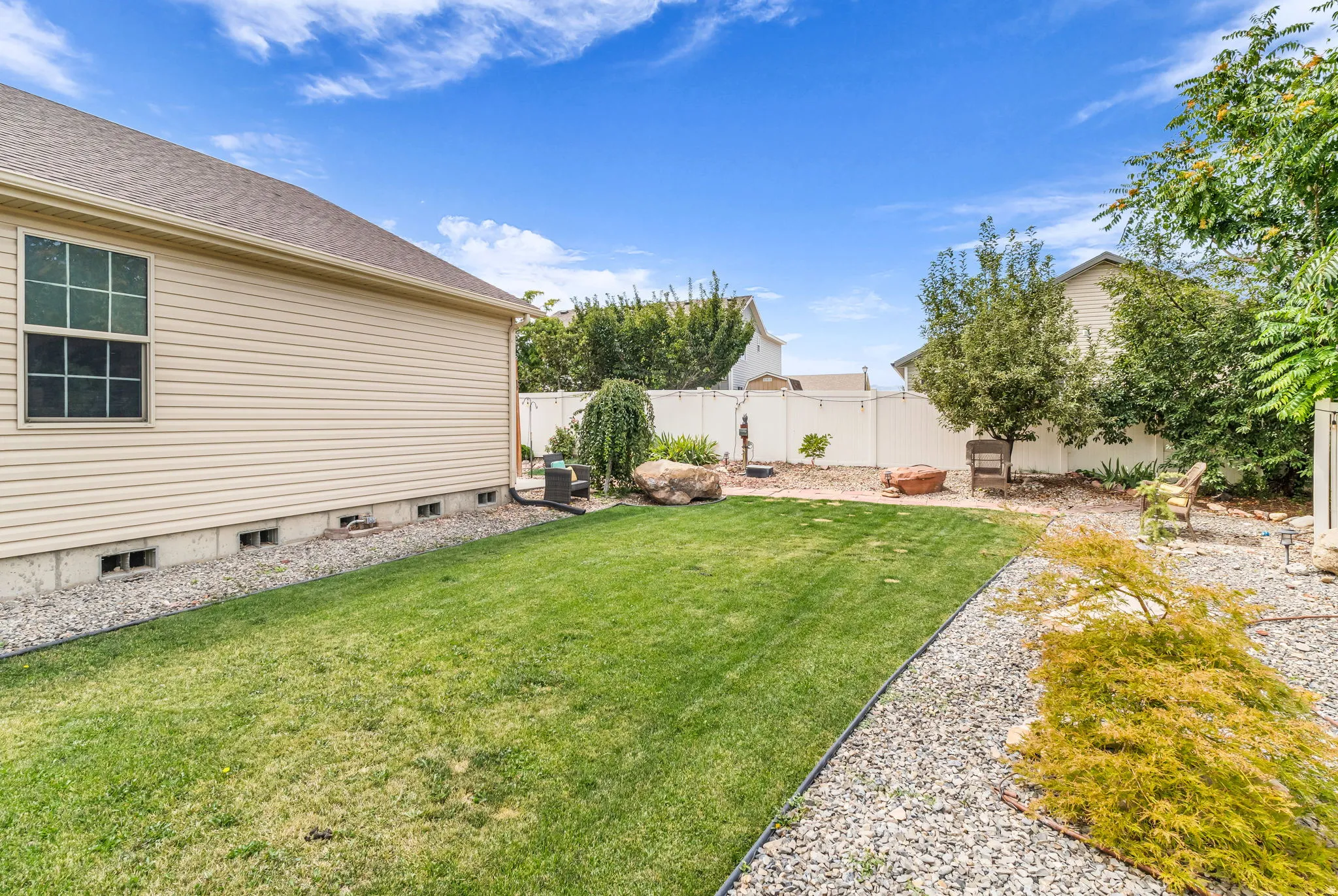 Expansive backyard featuring a manicured lawn, established landscaping, white privacy fencing, and gravel pathways