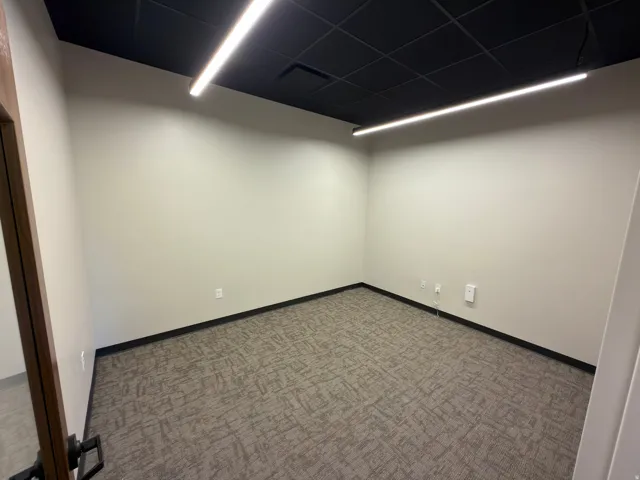 Recessed grid ceiling, linear overhead lighting, neutral wall paint, dark trim, and patterned carpet flooring