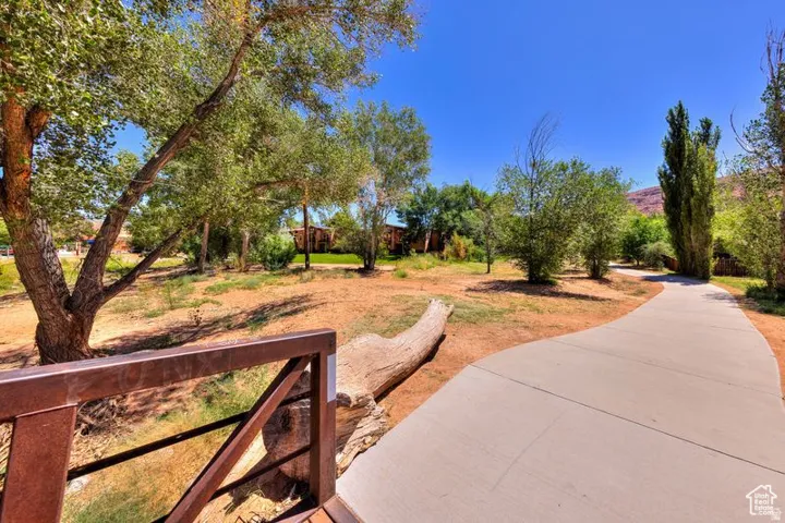 Paved pathway surrounded by mature trees, desert landscaping, and a distant mountain backdrop