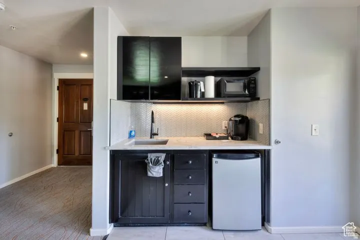 Compact kitchenette featuring black cabinetry, a white countertop, a tile backsplash, and a built-in sink