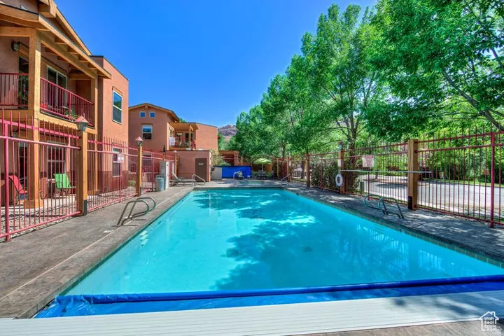 Rectangular swimming pool with integrated steps, surrounded by a concrete deck and a red metal fence