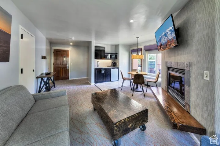 Integrated living space featuring a built-in fireplace with a stone surround, a dedicated dining area with a chandelier, and a kitchenette with a compact refrigerator