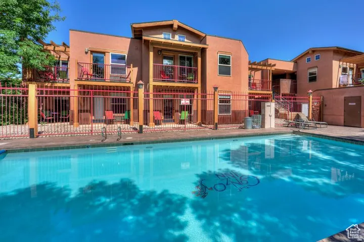 Outdoor swimming pool with integrated steps, surrounded by a metal fence with wooden posts, and multi-story buildings featuring balconies