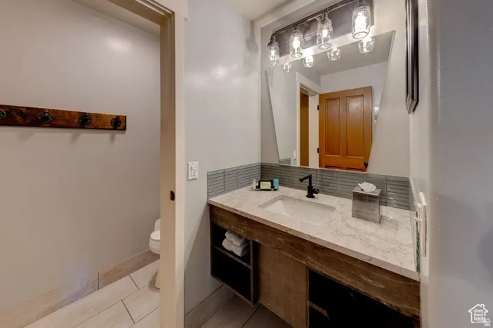 Vanity with a single basin, stone-finish countertop, wood-finish cabinetry with open shelving, matte black faucet, and a large wall-mounted mirror