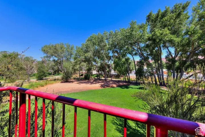 Balcony with red metal railing overlooking a landscaped area with grass, trees, and natural terrain