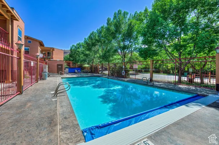 Outdoor swimming pool with concrete decking, surrounding perimeter fencing, and mature trees
