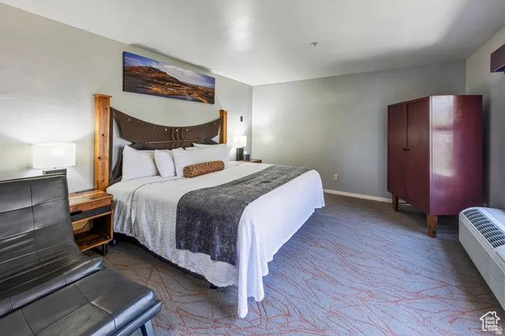 Spacious room with a decorative wooden headboard, light gray walls, and patterned carpet flooring