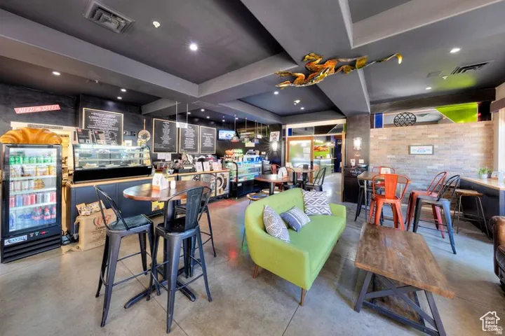Space featuring concrete flooring, a service counter with display cases, exposed brick accent wall, recessed lighting, and a prominent decorative ceiling fixture