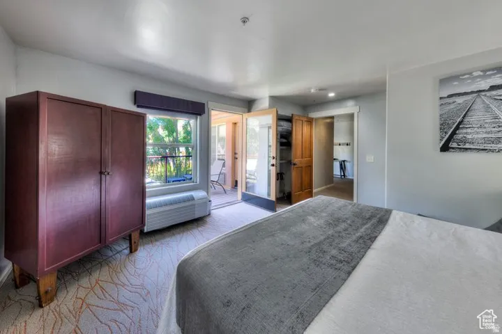 Room with patterned carpet, a built-in air conditioning unit, and glass French doors opening to an outdoor patio