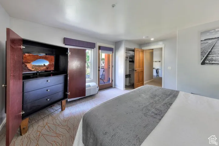 Spacious room featuring light gray wall paint, patterned carpeting, a built-in wood-finish armoire with drawers, and a glass-paneled door leading to an outdoor space