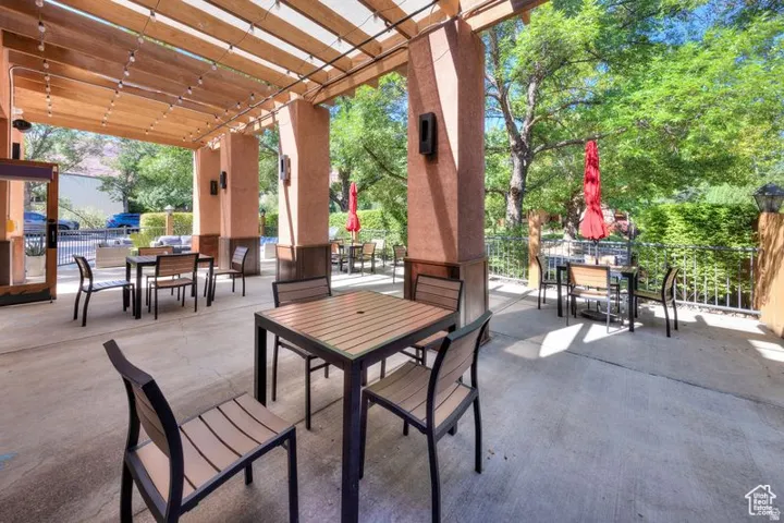 Expansive concrete patio featuring a wood pergola with string lighting, stucco-finished columns, and a wrought iron fence
