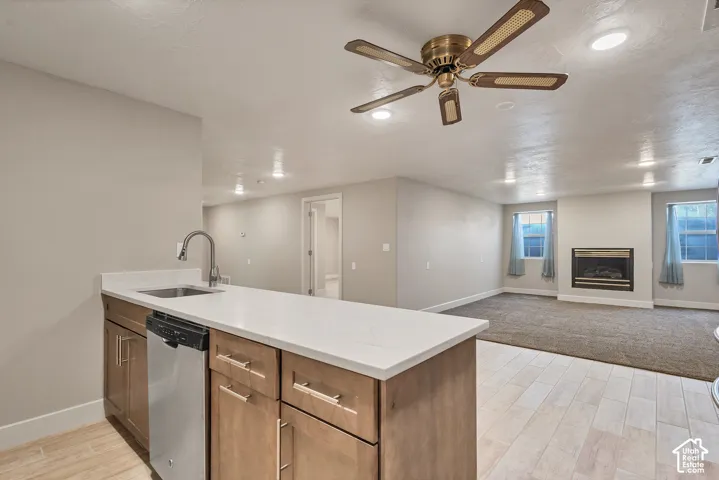 Kitchenette with a stainless steel sink, a dishwasher, wood-finish cabinetry, and solid surface countertops