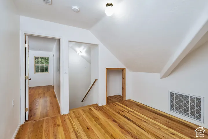 Hardwood flooring, painted white walls, sloped ceiling, recessed access opening, and a built-in vent