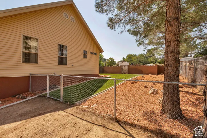 Light-colored siding exterior, chain-link fencing, mature tree, and landscaped yard with grass and wood chip ground cover