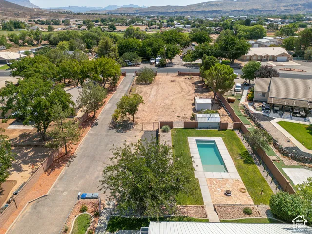 Rectangular swimming pool surrounded by a grass lawn, stone patio with a fire pit, and mature trees