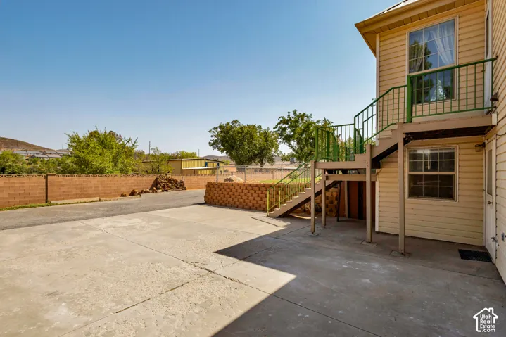 Concrete patio area with an exterior staircase featuring green railings, leading to an upper-level entry. Lower entry door to Basement.