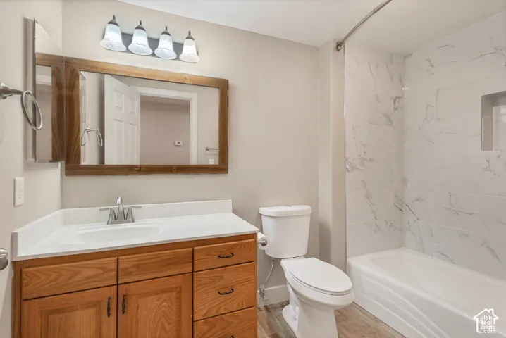 Bathroom featuring a wood-finish vanity with a white countertop, an undermount sink, a framed mirror, and a tiled shower with a built-in niche