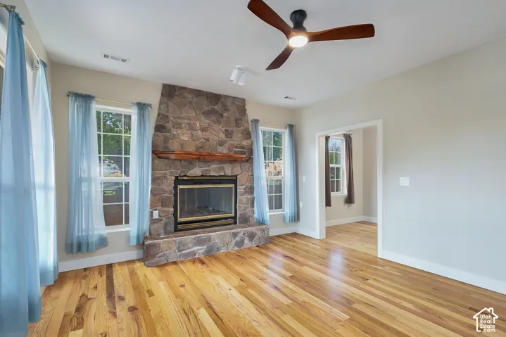 Stone-clad fireplace with a wood mantel, wood-finish flooring, and a ceiling fan